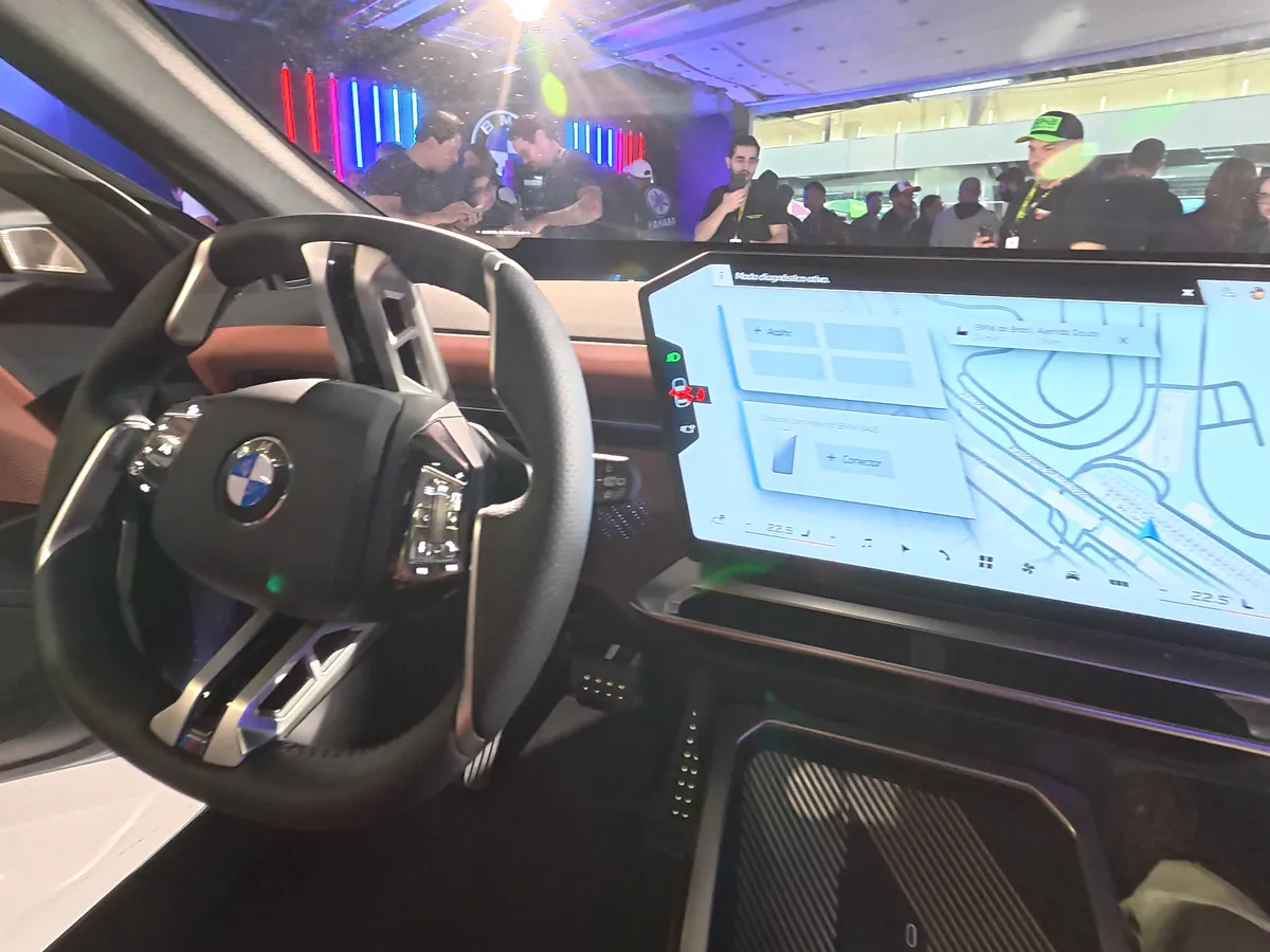 Interior do BMW iX3 com volante, painel digital e tela central curva exibindo o mapa de navegação