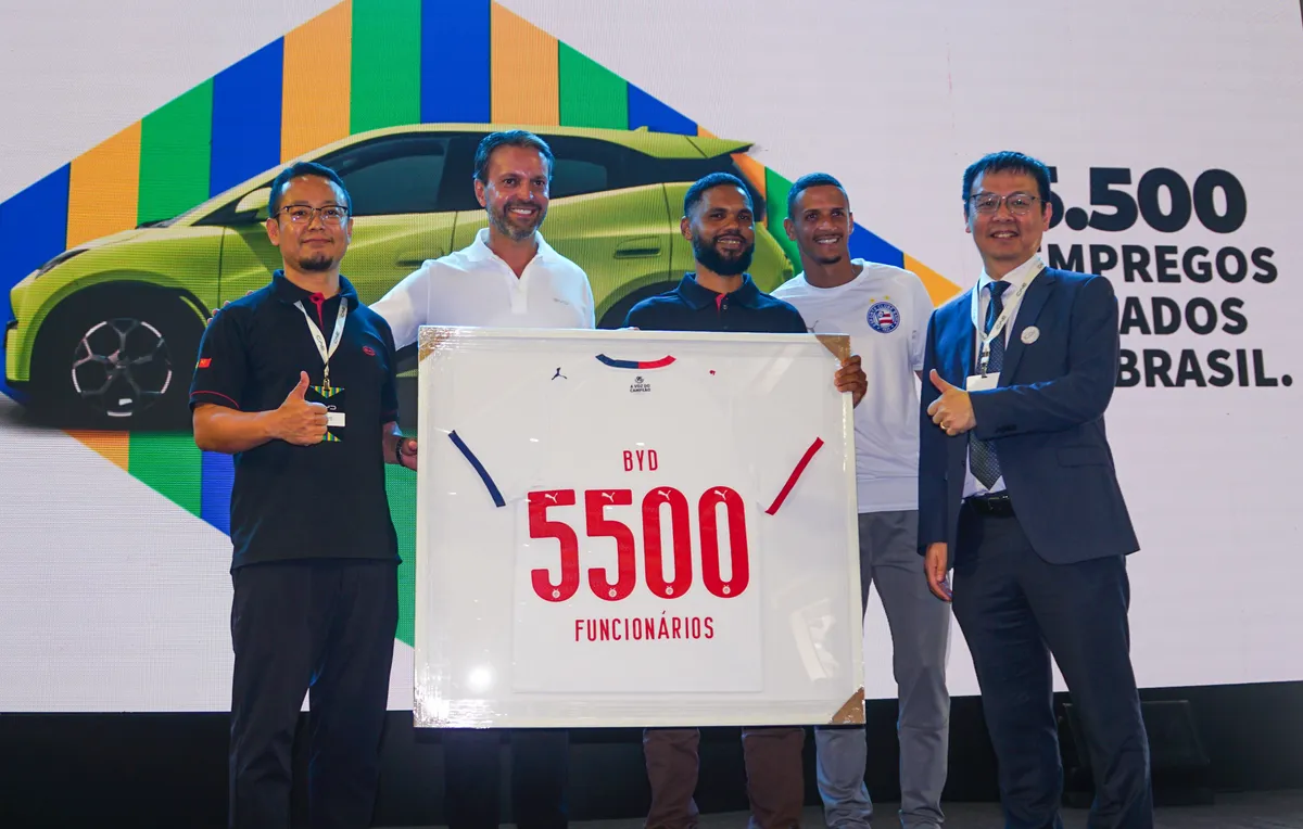 Executivos da BYD e convidados seguram camisa de futebol emoldurada com o número 5500 e a palavra funcionários