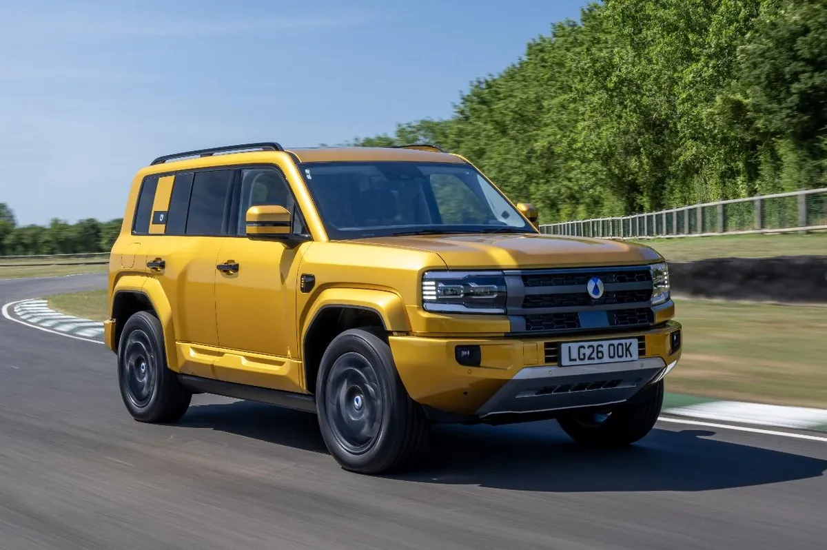 SUV Denza B5 amarelo em movimento numa pista de testes com vegetação ao fundo
