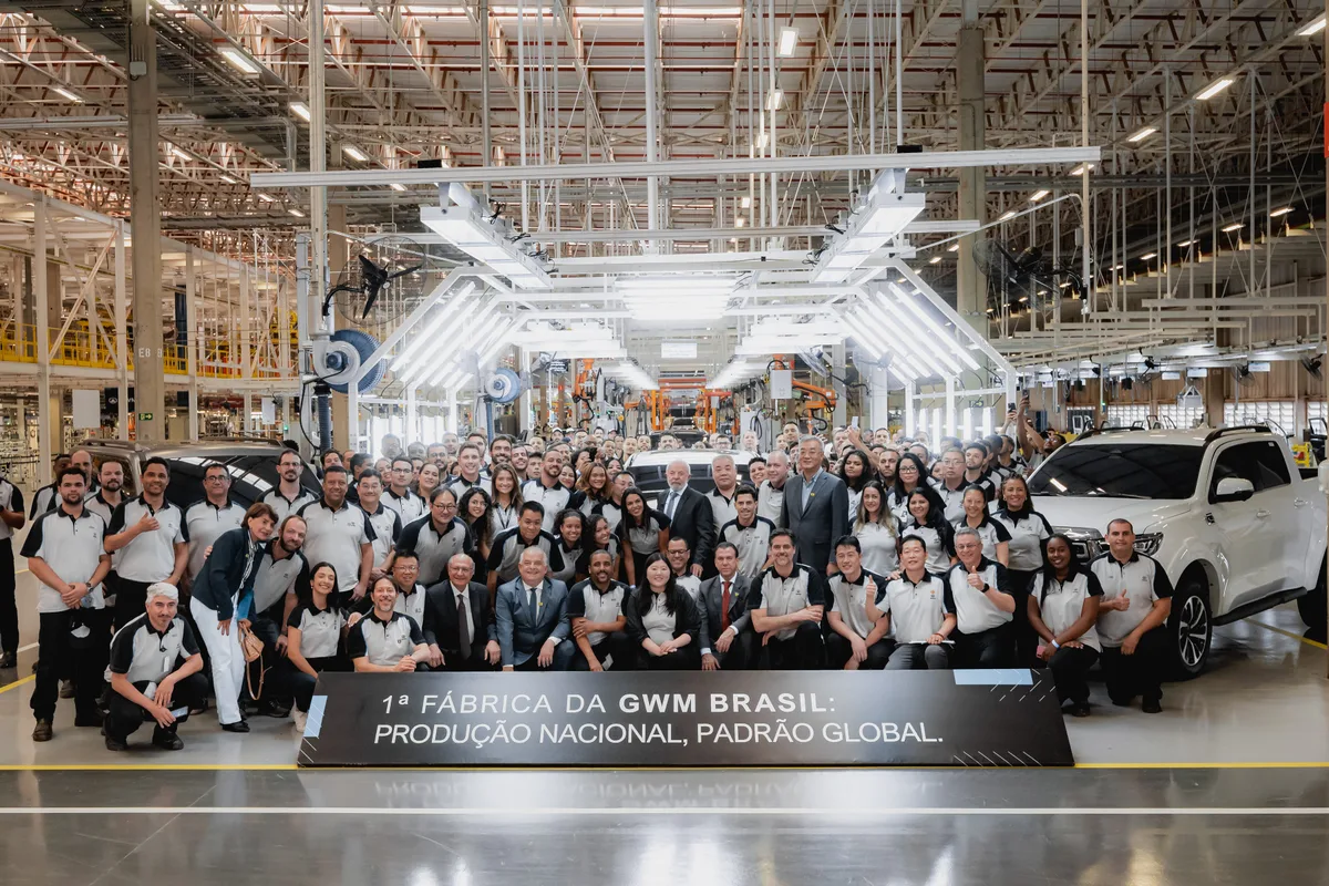 Equipe da GWM reunida na linha de montagem diante da placa 1ª Fábrica da GWM Brasil: produção nacional, padrão global