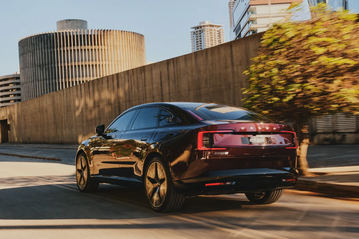 Traseira do Volvo ES90 vinho em movimento na cidade, com lanternas em formato de C acesas